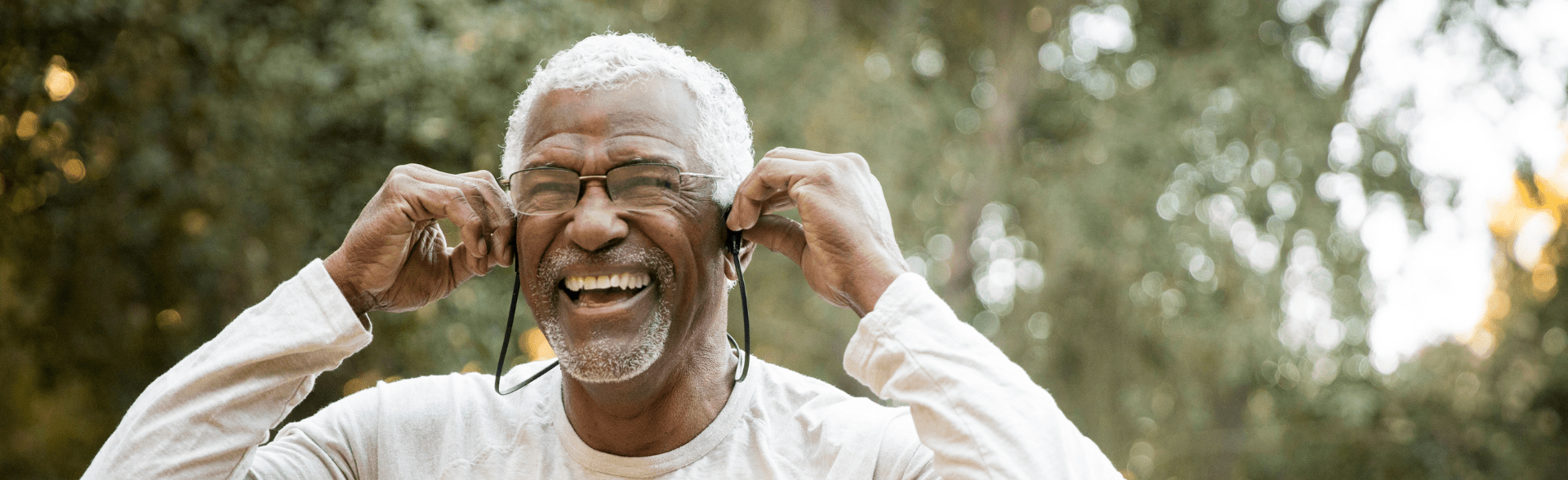 An older masc presenting person laughing. They are wearing glasses and a white long sleeved shirt.