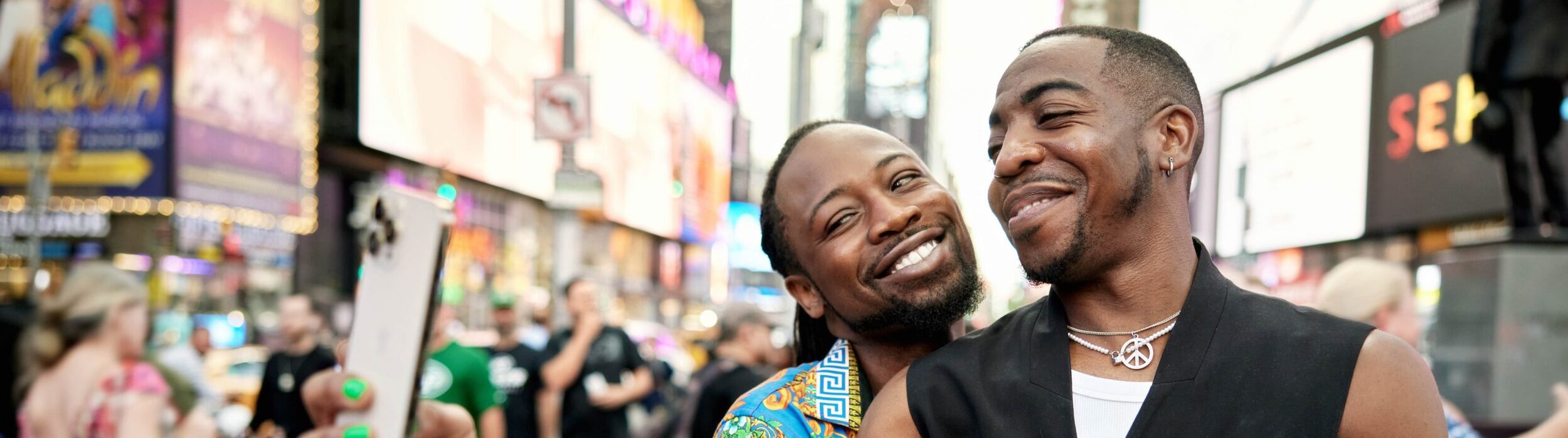 two black men, hugging, taking a selfie in Times Square
