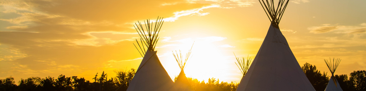 Indigenous tipis against an orange sunset. 