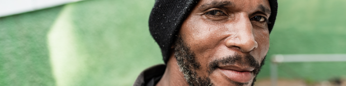 Man with a toque and a beard on a green background. Represents a person with lived experience. 